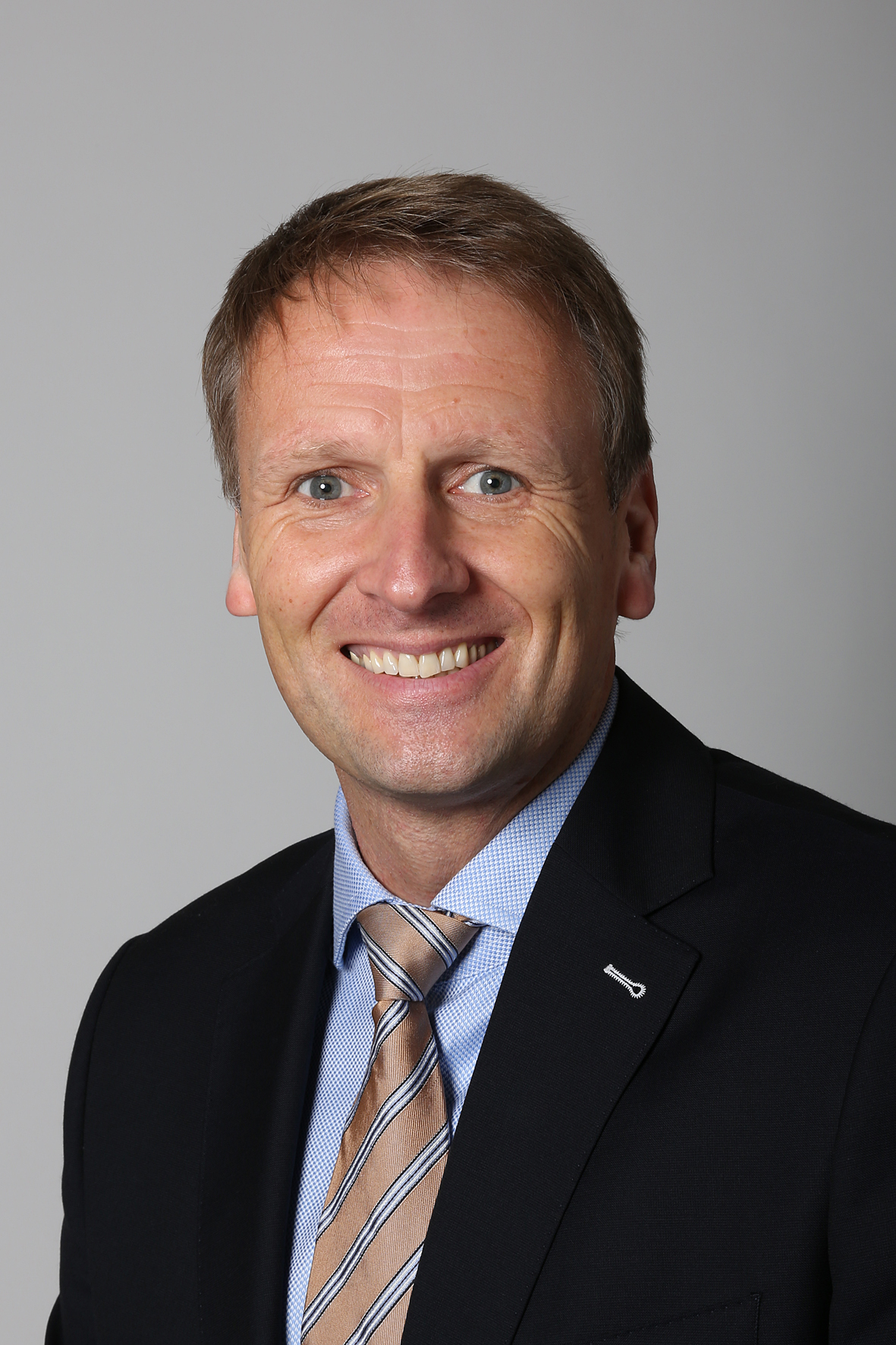 Stefan Kiefer, lächelnd, im Anzug und mit Krawatte, Porträtaufnahme.