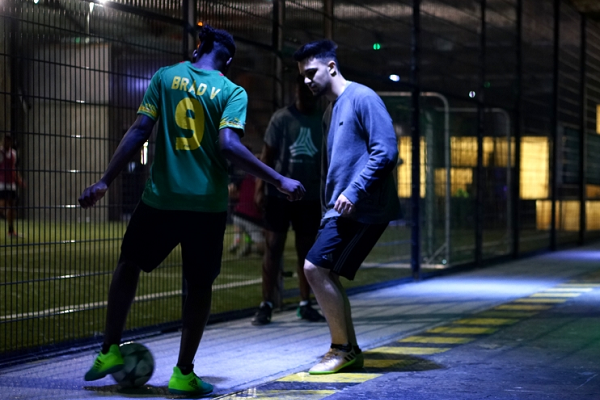 Two young men play soccer with each other in the dark.