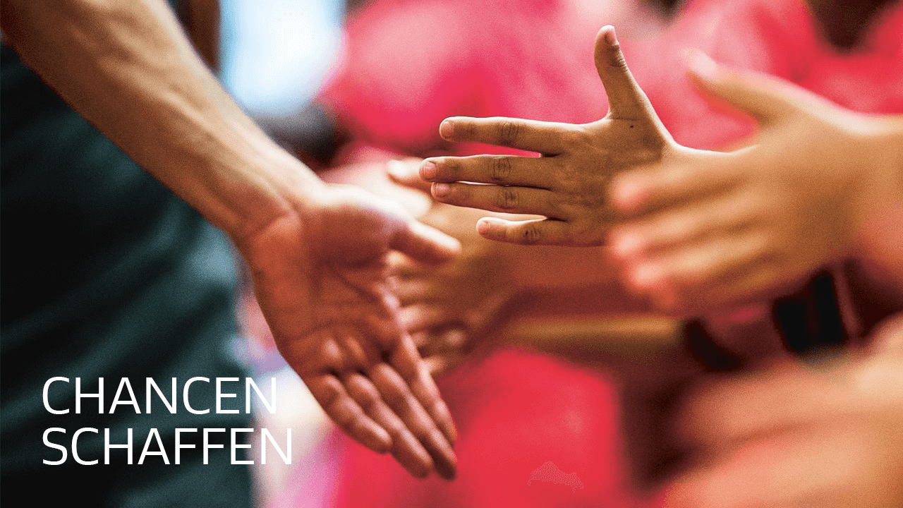 Hände verschiedener Hautfarben liegen ineinander, symbolisch für Gemeinschaft und Zusammenhalt. Im Vordergrund steht der Schriftzug "CHANCEN SCHAFFEN".