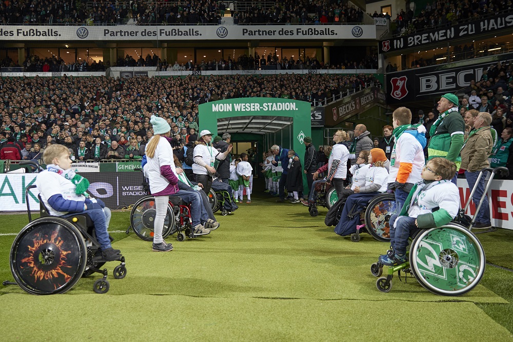 Aktionstag für Inklusion im Weserstadion: Kinder und Jugendliche mit und ohne Beeinträchtigung nehmen an einer gemeinsamen Fußballaktivität auf dem Rasen teil, unterstützt durch die DFL Stiftung und Aktion Mensch. Im Hintergrund sind zahlreiche Zuschauer auf den Tribünen zu sehen.