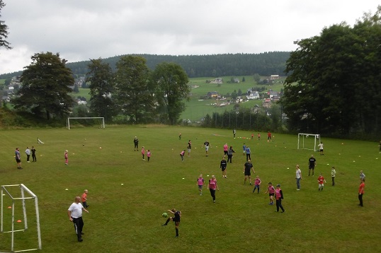 Auf einem Sportplatz spielen Kinder und Erwachsene zusammen Fußball.