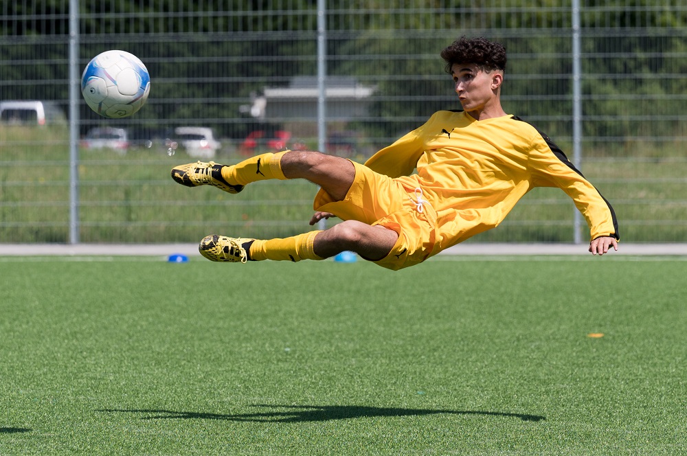Junge*r Fußballspieler*in in gelbem Trikot springt auf dem Fußballfeld und versucht den Ball mit der Fußspitze zu spielen – Impressionen vom regionalen „Willkommen im Fußball“-Cup 2021 in Duisburg.