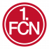 Logo 1. FC Nürnberg Eine Gruppe von Kindern und Jugendlichen steht in einer Turnhalle auf einer Bank und umarmt sich. Rechts steht ein Mann mit Sportkleidung und beobachtet die Szene. Im Hintergrund ist eine grüne Wand und ein Turnhallenfußboden zu sehen. Das Bild stammt von einem Projekt der DFL Stiftung "Fußball trifft Kultur" an einer Schule in Frankfurt am Main.