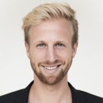 Talkrunde mit mehreren Personen, die auf Barhocker sitzend diskutieren. Im Hintergrund eine dunkle Bühne und das Vereinslogo von Schalke 04.