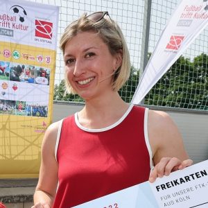Fußballstadion mit voll besetzten Rängen, im Vordergrund Spieler in Teamkleidung, dahinter ein Banner mit den Logos der DFL Stiftung und der Deutschen Sporthilfe und dem Schriftzug "10 Jahre Spitzensport verbindet".