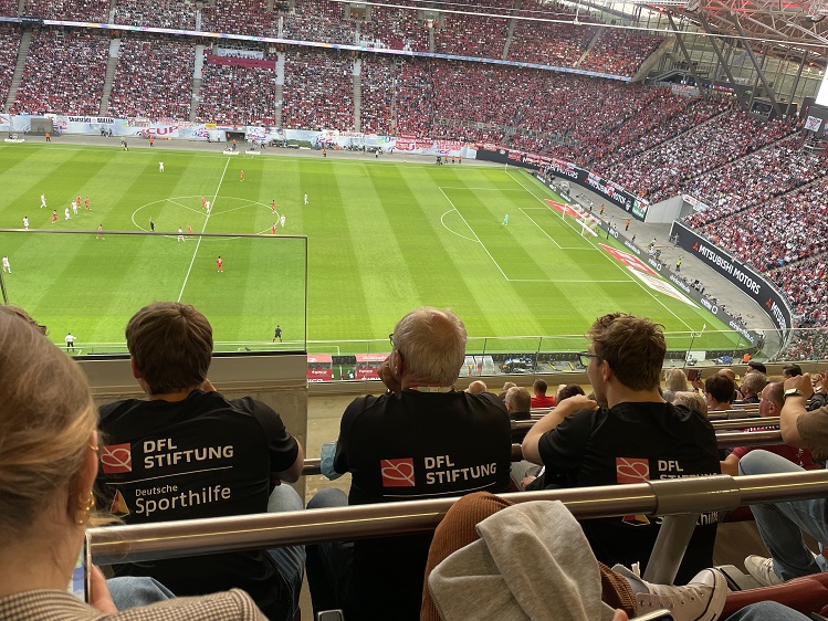 Neue Kuratoren der DFL Stiftung sitzen an einem weißen Tisch auf der Bühne während des Neujahrsempfangs "ANSTOSS 2019" in Frankfurt. Von links sind ein Mann mit Mikrofon, ein Mann im Anzug, ein weiterer Mann, eine Frau und ein weiterer Mann zu sehen. Im Hintergrund ist das Logo der DFL Stiftung sowie die Aufschrift "ANSTOSS 2019" zu erkennen.
