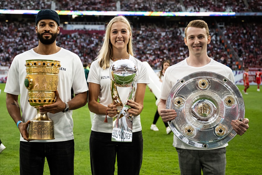 Banner mit der Aufschrift "Nie wieder!" und "Erinnern reicht nicht" im Stadion während einer Fußballveranstaltung, im Hintergrund zahlreiche Zuschauer.