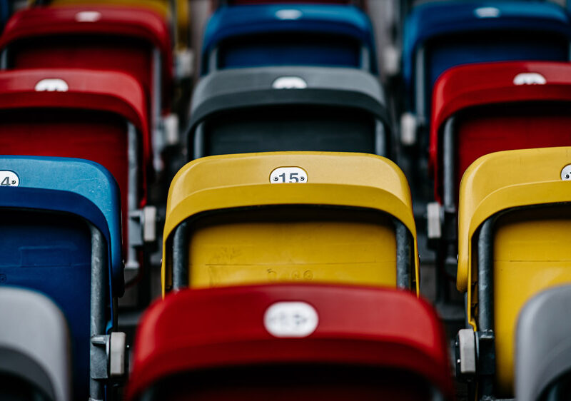 Leere Stadiontribünen in verschiedenen Farben, symbolisch für das Thema Hassrede und Diskriminierung im Fußball.