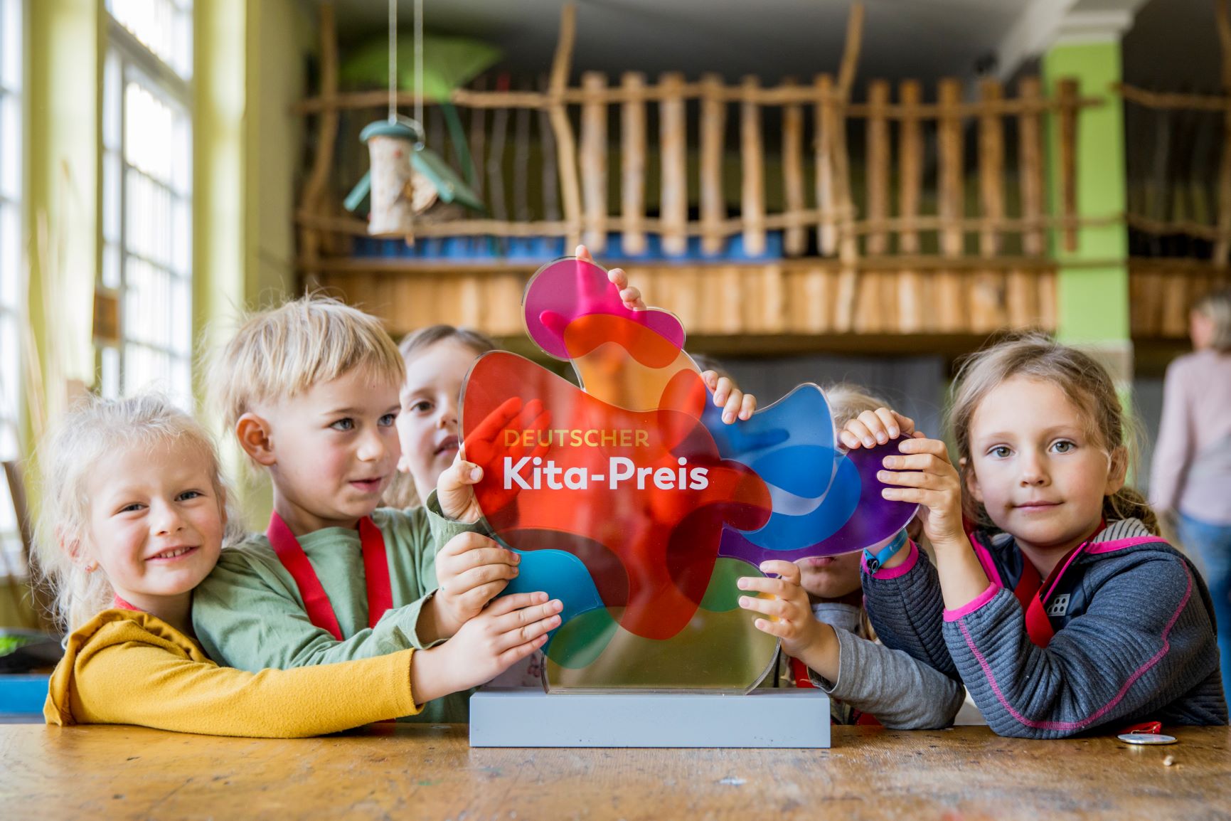 Eine Gruppe von Kindern steht erwartungsvoll vor einer farbenfrohen Trophäe mit der Aufschrift "Deutscher Kita-Preis".