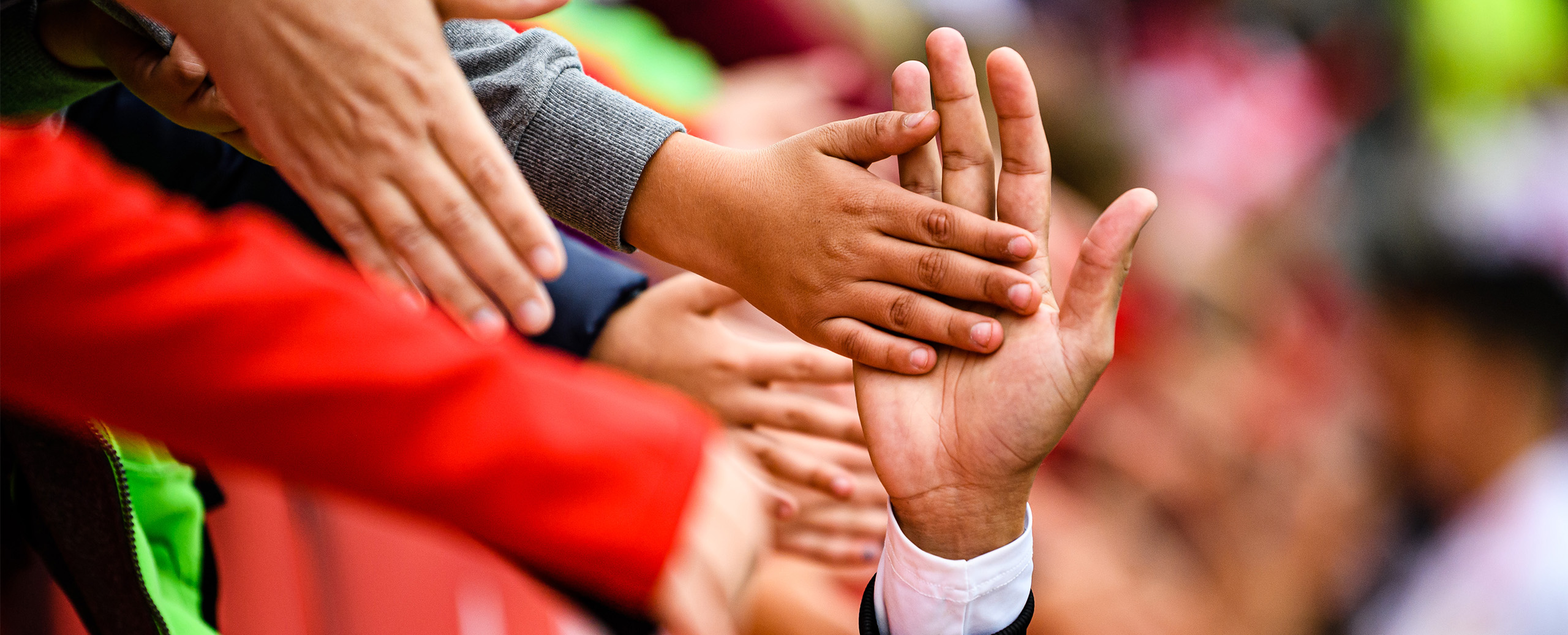 Kinder klatschen am Spielfeldrand eine Hand eines Fußballers ab.
