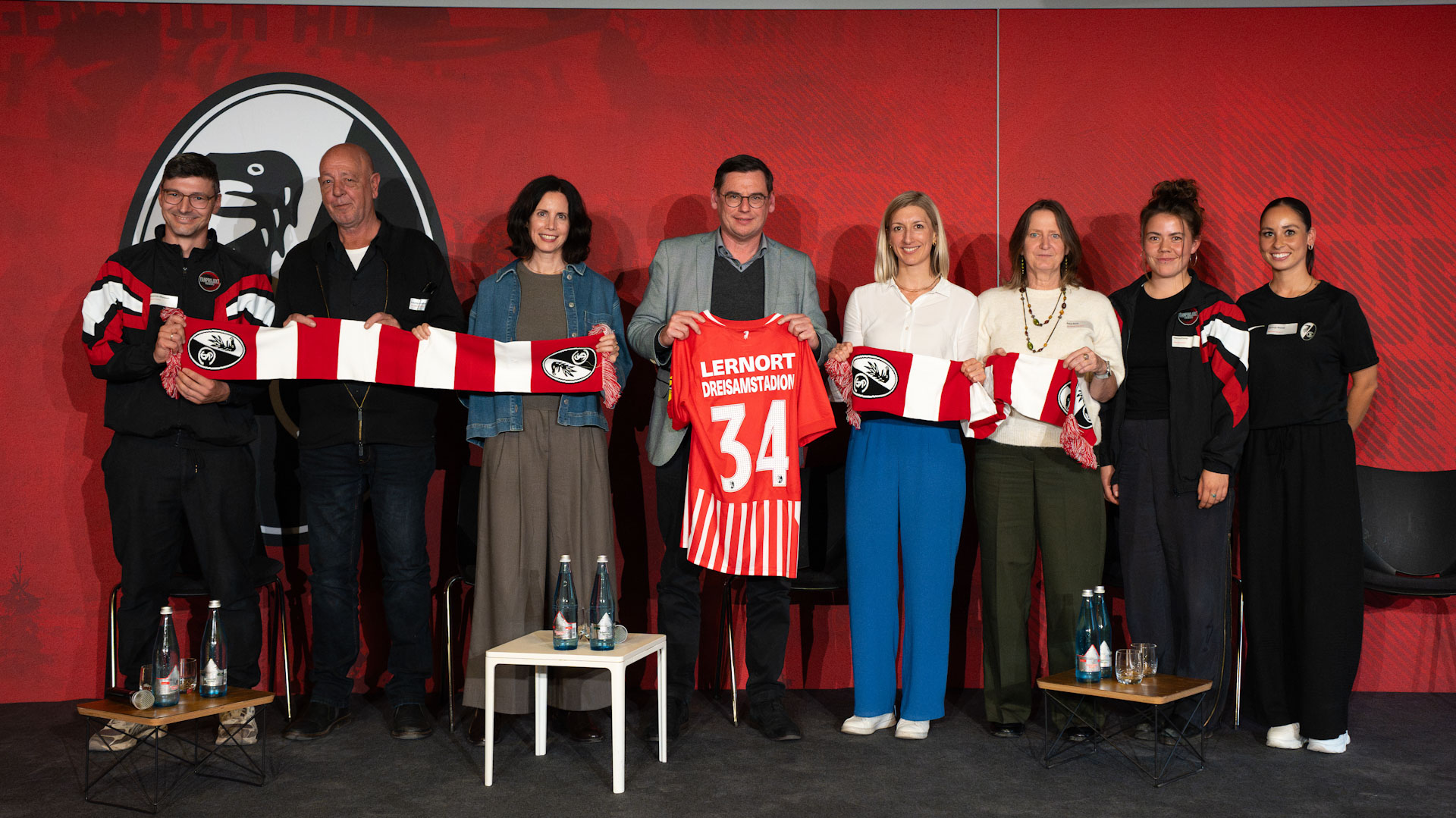 Menschen halten ein Trikot mit der Nr. 34 sowie einen Schal des SC Freiburg in die Kamera